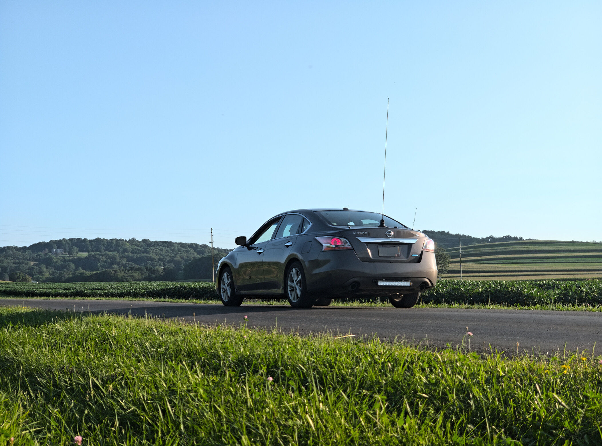 A brown sedan on a rural road with 3 antennas on the trunk and other technology modifications.