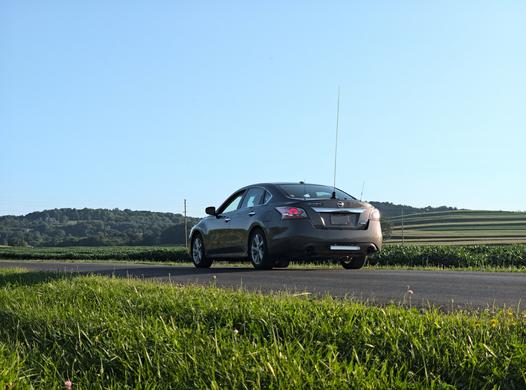 A picture of a brown 2013 Nissan Altima parked on a rural road, with 3 antennas of varying length on the trunk